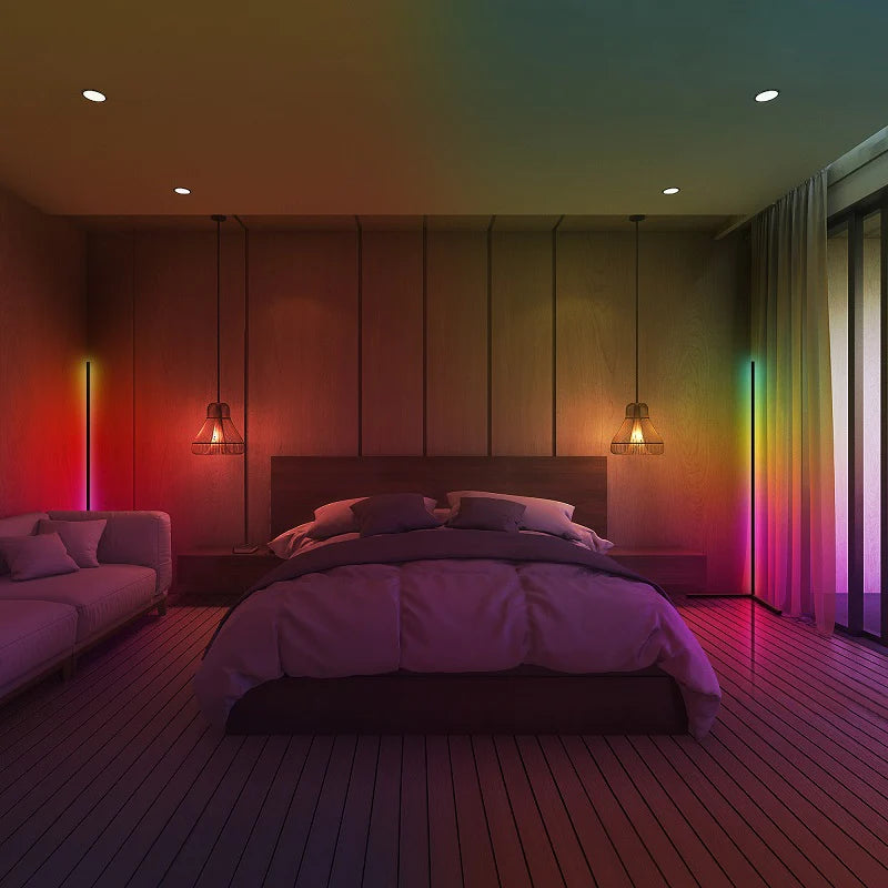 A king-sized bed in the center of a large modern primary bedroom suite lit in rainbow color by Enlights LED vertical strip lamps on either side of the room in the corners. 