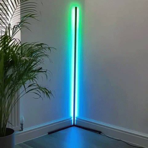 A video of the Enlights LED vertical strip corner lamp cycling slowly in rainbow colors in the corner of a white room with a plant. 